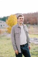 Young smiling man stands against the background of a yellow tree in a clearing photo