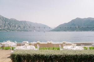 Festive served tables stand on a wooden terrace near the fence above the sea with a view of the mountains photo