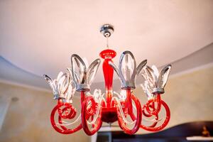 Red chandelier with swirls and flower-shaped shades hangs from the ceiling photo