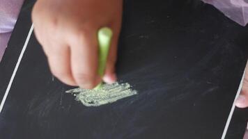 Child drawing with chalk on a black surface in bright sunlight video