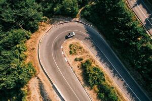 White convertible turns along a serpentine road in the mountains. Drone photo