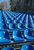 Rows of blue chairs are arranged in an amphitheater near an ancient stone building photo