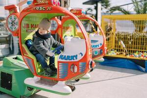 Little girl sits at the helm of a toy helicopter on the playground and looks away photo