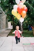 Little girl with a bunch of colorful balloons walks through a green garden photo