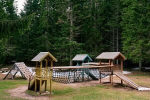 Wooden playground with an obstacle course and a climbing wall in a green forest photo