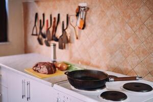 Frying pan stands on the stove against the background of a raw tenderloin and vegetables on the table photo