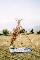 Boho-style wedding arch stands on a green lawn above a bedspread with pillows photo