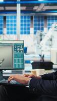 Vertical Employee in renewable energy based factory using laptop to review performance of robot arms placing solar panels. Specialist inspects machinery placing solar cells on conveyor belts, camera A video