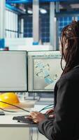 Vertical Programmer in photovoltaics factory using PC to update software of robot arms placing solar panels on assembly lines. Woman coding on computer, upgrading solar plant machinery, camera A video