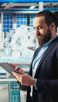 Vertical Portrait of engineer in photovoltaics factory using tablet to diagnose malfunctioning systems. Solar panels manufacturing plant worker reduces downtime and maintains operational reliability, camera A video