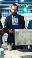 Vertical Portrait of smiling inspectors in photovoltaics factory reviewing performance of robot arms placing solar panels on assembly lines. Team of happy supervisors inspecting solar plant machinery, camera A video