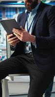 Vertical Photovoltaics factory employee uses tablet to review performance of robot arms placing solar panels on assembly lines. Specialist sitting on desk uses device to inspect solar plant machinery, camera A video