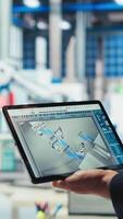 Vertical Engineer in photovoltaics factory uses tracking software on tablet to review performance of robot arms manufacturing solar panels. Expert uses device to inspect solar plant machinery, camera A closeup video