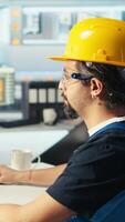 Vertical Photovoltaics factory engineer wearing yellow hardhat analyzing data, reviewing system metrics. Solar panels plant technician troubleshooting technical issues using computer software, camera A video