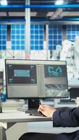 Vertical Photovoltaics factory worker using PC to monitor performance of robot arms placing solar panels on assembly lines. Expert at computer desk looking on screen, inspecting solar plant machinery, camera A video