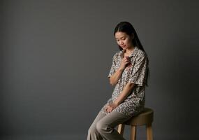 A woman sitting on a stool with her hand on her chest photo