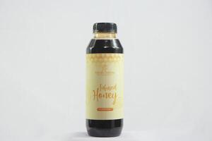 Freshs farm honey in a glass bottle, sealed with a cork, placed on a wooden table with honeycomb and blooming flowers photo