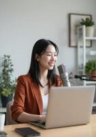 A woman in a business suit is sitting at a desk with a laptop and microphone photo
