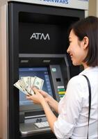 A woman is holding money in front of an atm machine photo