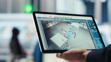 Engineer in photovoltaics factory uses tracking software on tablet to review performance of robot arms manufacturing solar panels. Expert uses device to inspect solar plant machinery, camera B closeup video