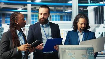 Portrait of smiling inspectors in photovoltaics factory reviewing performance of robot arms placing solar panels on assembly lines. Team of happy supervisors inspecting solar plant machinery, camera B video