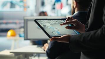 Solar panels plant employee uses CAD software on tablet to optimize layouts. Photovoltaics factory worker doing arrangements for maximum energy output using device, camera B close up video