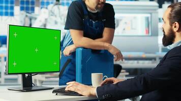 Photovoltaics factory manager talking with employee, using green screen PC to monitor performance of robot arms manufacturing solar panels. Supervisor chatting with worker, sitting at mockup computer video