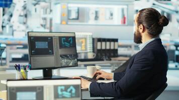 Photovoltaics factory worker using PC to monitor performance of robot arms placing solar panels on assembly lines. Expert at computer desk looking on screen, inspecting solar plant machinery, camera B video