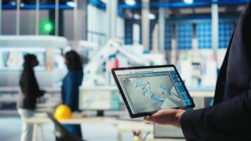 Engineer in photovoltaics factory uses tracking software on tablet to review performance of robot arms manufacturing solar panels. Expert uses device to inspect solar plant machinery, camera A closeup video