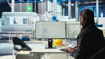 Programmer in photovoltaics factory using PC to update software of robot arms placing solar panels on assembly lines. Woman coding on computer, upgrading solar plant machinery, camera A video