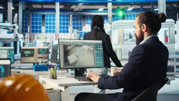 Engineer in photovoltaics factory using PC screen to diagnose malfunctioning systems. Solar panels manufacturing plant worker at computer desk maintaining system operational reliability, camera A video