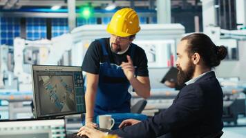 Photovoltaics factory manager showing engineer on PC screen how to adjust system parameters. Specialist showing staff member how to optimize energy supply in solar panel manufacturing plant, camera B video