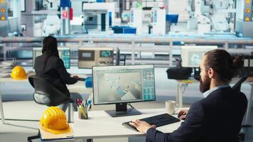 Photovoltaics factory worker drinks coffee, monitoring performance of robot arms placing solar panels on assembly lines. Man enjoys beverage at computer desk, inspecting solar plant machines, camera A video