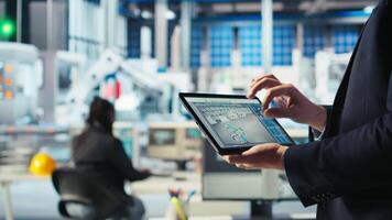 Photovoltaics factory technician monitoring system performance on tablet. Solar panels manufacturing plant worker using device to track energy production and efficiency, camera A close up video