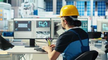 Photovoltaics factory engineer using PC to test robot arms placing solar panels on assembly lines. Professional sitting at computer desk inspecting solar plant heavy machinery units, camera B video