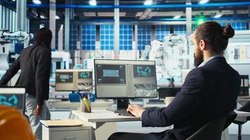 Photovoltaics factory worker using PC to monitor performance of robot arms placing solar panels on assembly lines. Expert at computer desk looking on screen, inspecting solar plant machinery, camera A video