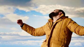 Joyful hiker triumphant at the mountain top dancing and cheering, soaks in the peaceful atmosphere and fresh air. Enjoying the scenic background of towering peaks and clouds. Camera B. video
