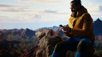 Trekker enjoys a quiet moment in the mountains scrolling phone app, where the high altitude air and breathtaking view encourage mindfulness. Relaxation and self improvement. Camera A. video