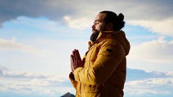 Young explorer reaching the mountain peak and meditating at the top, doing a zen meditation with calm and mindfulness. Happy content hiker loving nature for self care. Camera B. video