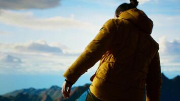 Determined climber pauses to admire the scenic view with mountains and a vast sky create a breathtaking backdrop. Man hiking for exploration and adventure in the nature. Camera B. video