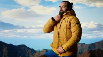 Determined traveler enjoys the solitude of a mountain summit, where the panoramic view represents adventure and personal growth. Hiker feeling cold on the windy mountain top. Camera B. video