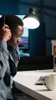 Vertical African american specialist closing the monthly balance with a show on headset, working remotely while he listens to his favorite podcast. Managing expenses and insurances from home. Camera B. video