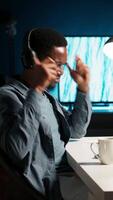 Vertical Young casual guy listening to a podcast while he works on freelance job at home, enjoys multitasking with headphones. Man solving tasks and paying attention to webinar discussion. Camera B. video