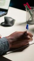 Vertical African American person working remotely and drafting project notes, organizing files and browsing web for relevant information. Comfortable home office setup for telework productivity. Camera B. video