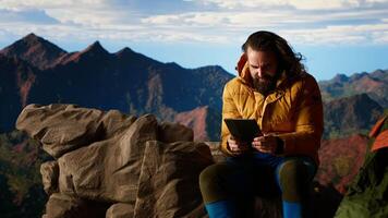 Male hiker struggles to work online in windy conditions on a remote mountain peak. Battling weak signals and cold weather, explorer is obsessed with technology and the internet. Camera B. video
