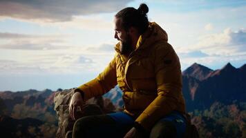 Victorious hiker relaxing at the mountain summit after climbing the top, proud of personal accomplishment. Young man sitting on the rocks and enjoying the peaceful surroundings. Camera A. video