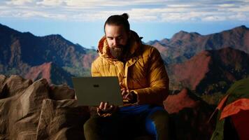 Nature lover workaholic always connected to the internet and scrolling on laptop, enjoying strong signal on a mountain top with a breathtaking landscape. Uninterrupted work. Camera B. video