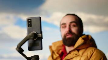 Vlogger recording a with a smartphone on a tripod capturing a panoramic view of the mountains from a rocky peak. Content creator shares his passion for travel and nature. Camera B. video