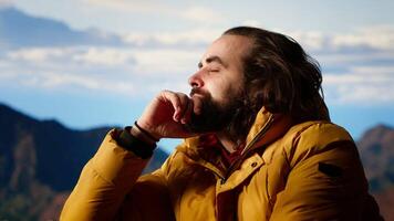 Male active trekker admiring the beautiful mountain range valley but dealing with cold winds, struggling with dangerous windy weather in his campsite. Wanderlust in nature. Camera B. video