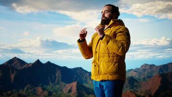 Adventure seeker doing a meditation pose on top of the mountain, successfully climbing the hill and enjoying the scenic landscape. Young calm zen traveler hiking and meditating. Camera A. video